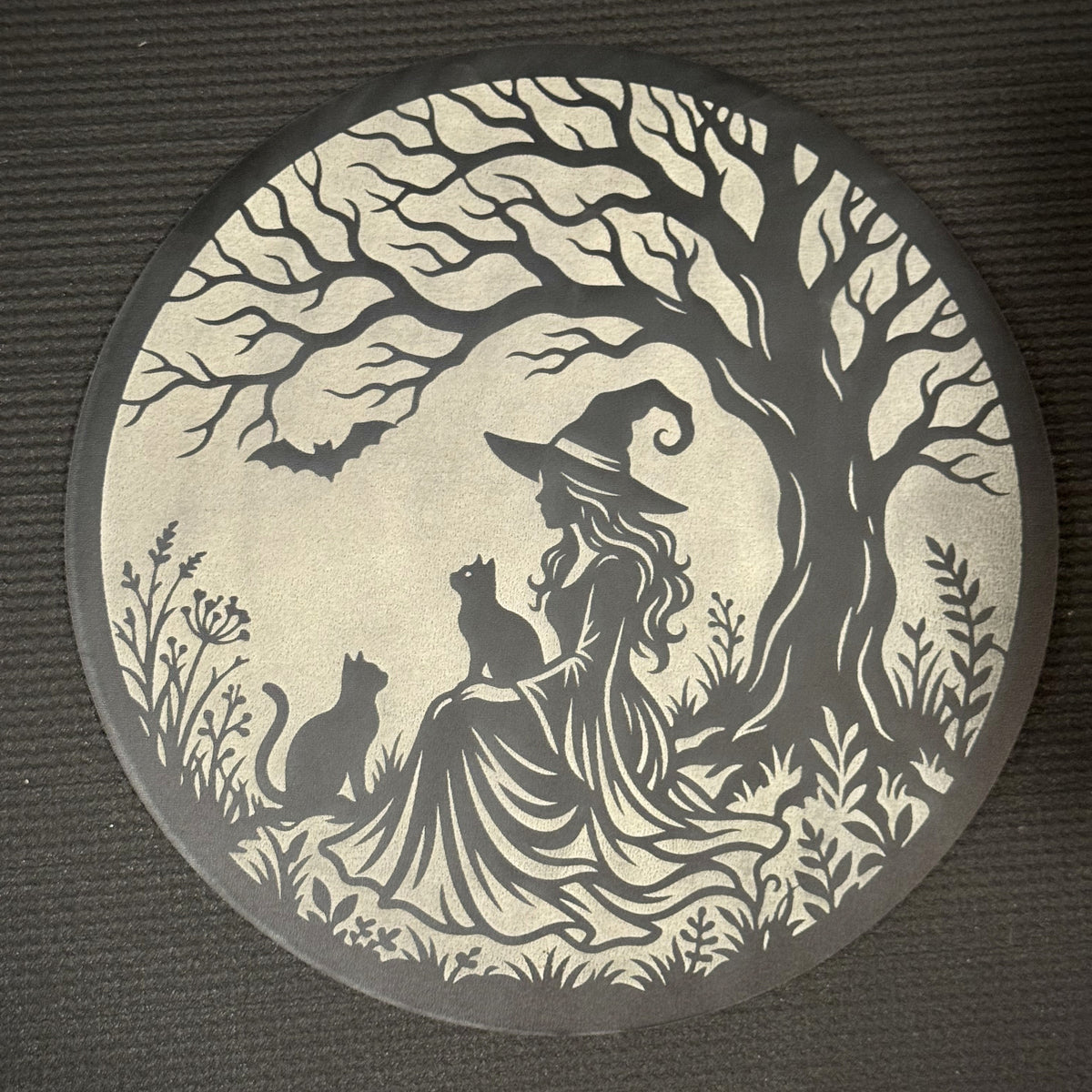 Under the Witching Tree in layered Creatorally wood — 11 inch round wall art, dark top layer cut back to a pale cream layer, showing a witch seated beneath a twisted tree with two cats and a bat