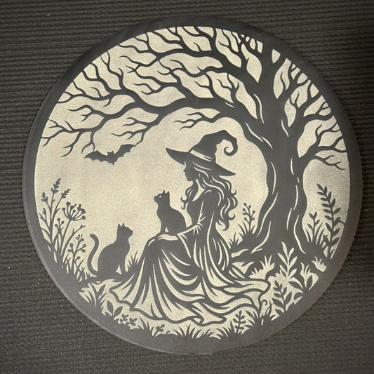 Under the Witching Tree in layered Creatorally wood — 11 inch round wall art, dark top layer cut back to a pale cream layer, showing a witch seated beneath a twisted tree with two cats and a bat